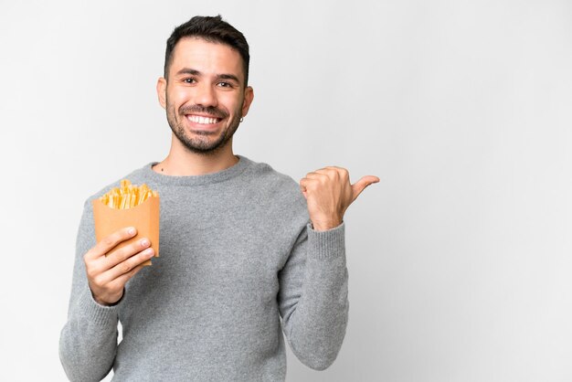 Young caucasian man holding fried chips over isolated white background pointing to the side to present a product