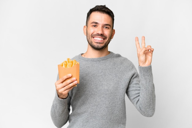 Young caucasian man holding fried chips over isolated white background smiling and showing victory sign