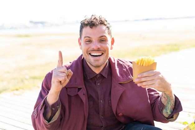 Giovane uomo caucasico che tiene patatine fritte all'aperto indicando una grande idea