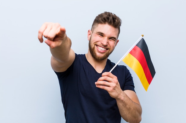 Young caucasian man holding a germany flag cheerful smiles pointing to front.