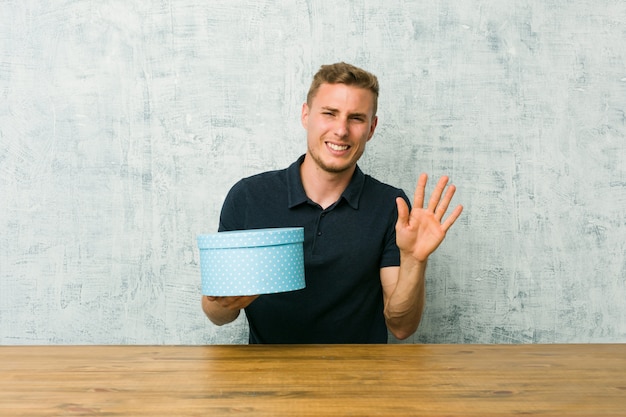 Young caucasian man holding a gift box on a table rejecting someone showing a gesture of disgust.