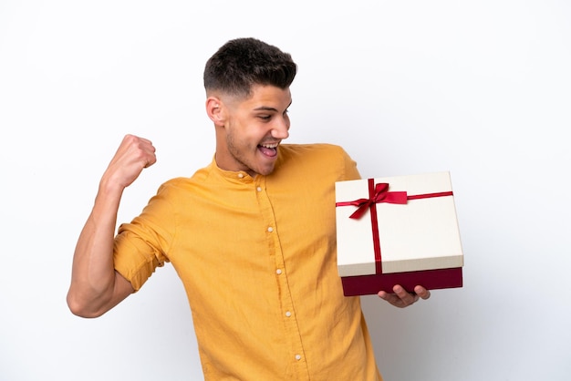 Young caucasian man holding a gift isolated on white background celebrating a victory