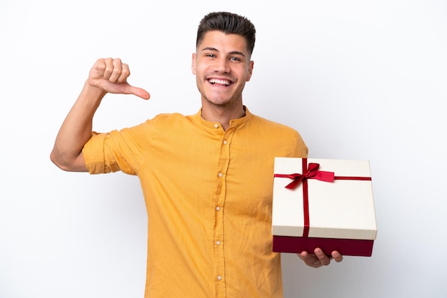 Young caucasian man holding a gift isolated on white background proud and selfsatisfied