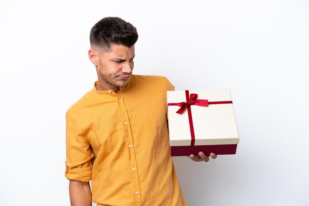 Young caucasian man holding a gift isolated on white background with sad expression