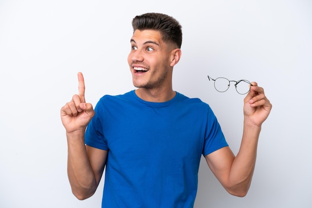 흰색 배경에 격리된 안경을 들고 손가락을 들어올리면서 해결책을 실현하려는 백인 청년
