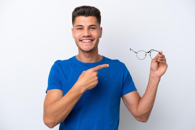 Young caucasian man holding glasses isolated on white background and pointing it