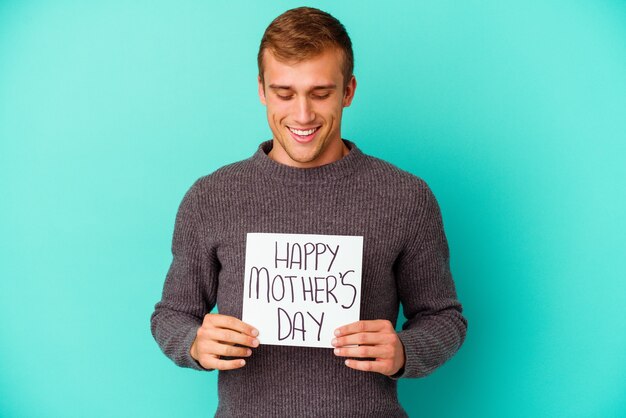 Young caucasian man holding a happy mothers day isolated on blue wall