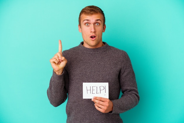 Young caucasian man holding a help placard isolated on blue wall having some great idea, concept of creativity.