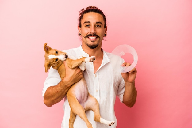 Young caucasian man holding his puppy and protection collar isolated on pink background