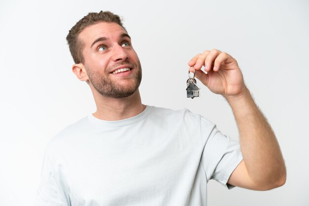 Young caucasian man holding home keys isolated on white background celebrating a victory