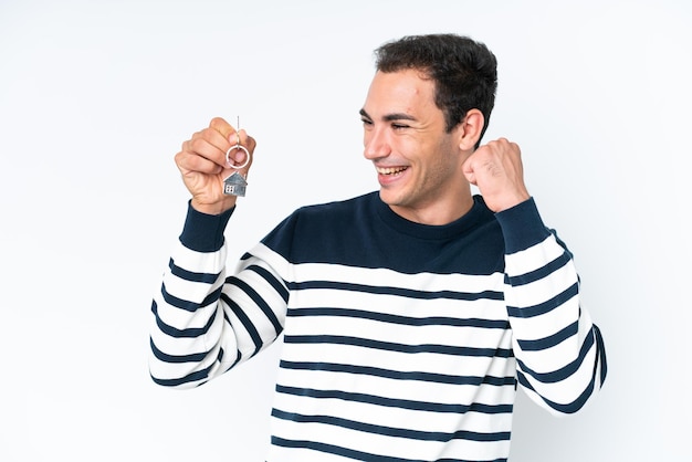 young caucasian man holding home keys isolated on white background celebrating a victory