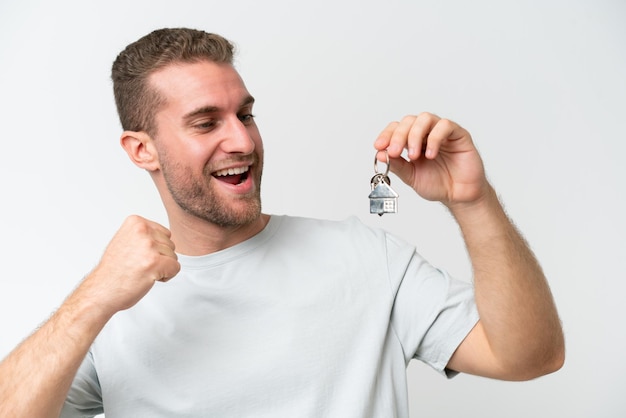 Young caucasian man holding home keys isolated on white background showing ok sign with fingers