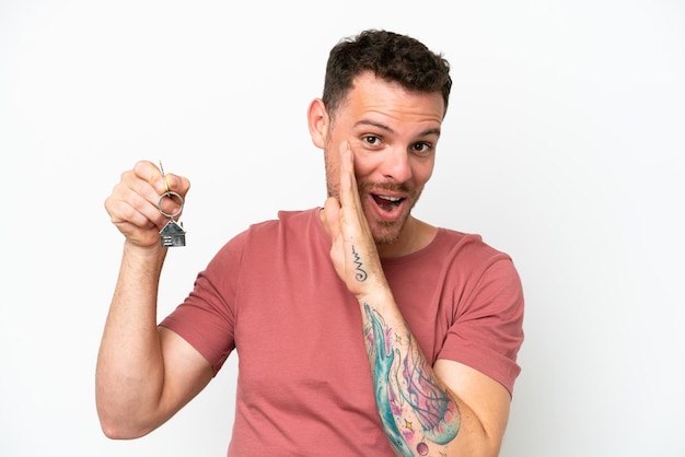 Young caucasian man holding home keys isolated on white background whispering something