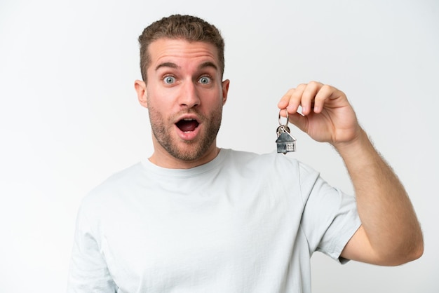 young caucasian man holding home keys isolated on white background with surprise facial expression