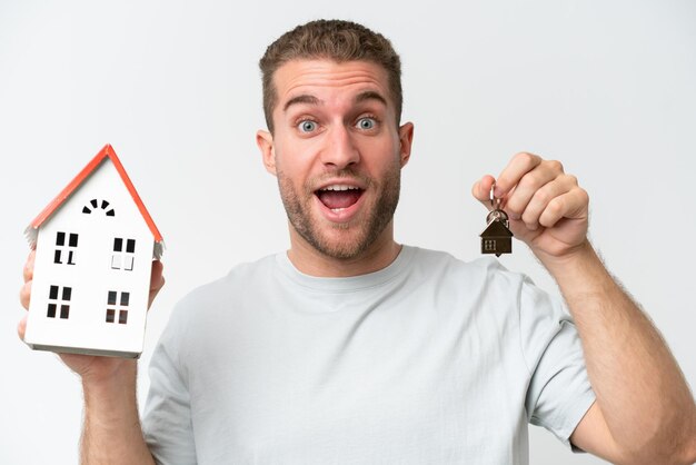 Young caucasian man holding home keys and toy house isolated on white background