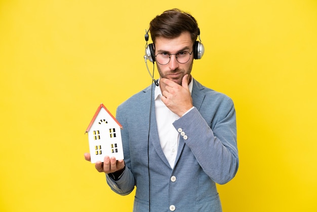 Young caucasian man holding a house isolated on white background thinking