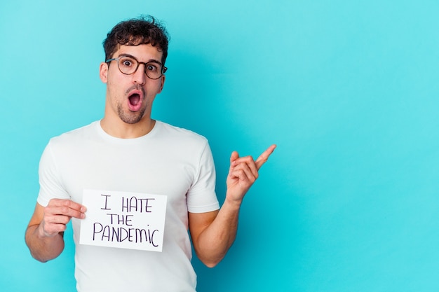 Young caucasian man holding a I hate the pandemic placard isolated pointing to the side