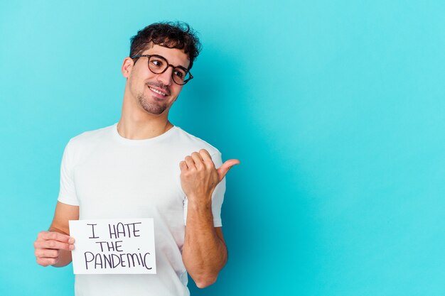 Foto giovane uomo caucasico che tiene in mano un odio i punti isolati del cartello pandemico con il dito del pollice lontano, ridendo e spensierato.