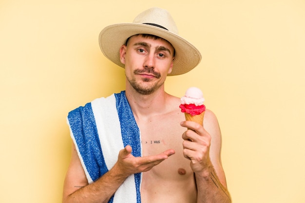 Young caucasian man holding an ice cream isolated on yellow background