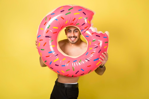 Young caucasian man holding an inflatable donut isolated on yellow background