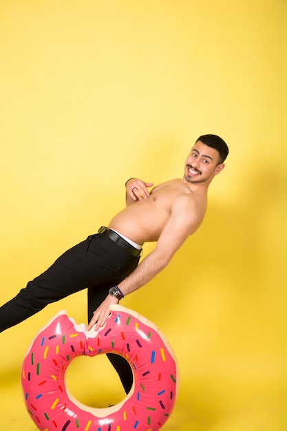 Young caucasian man holding an inflatable donut isolated on yellow background