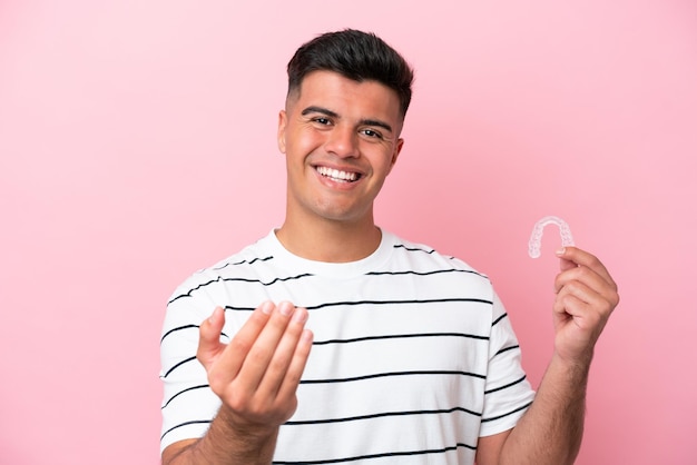 Young caucasian man holding invisaling isolated on pink background inviting to come with hand Happy that you came