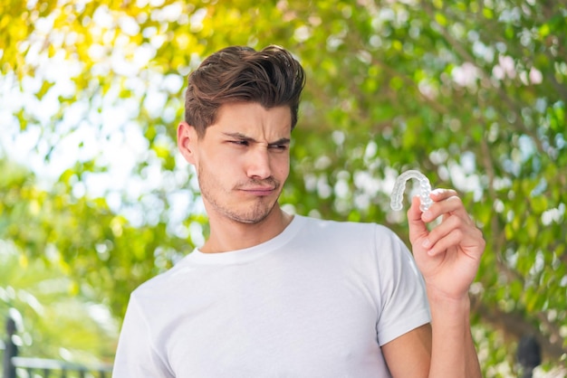 Young caucasian man holding invisible braces at outdoors with sad expression