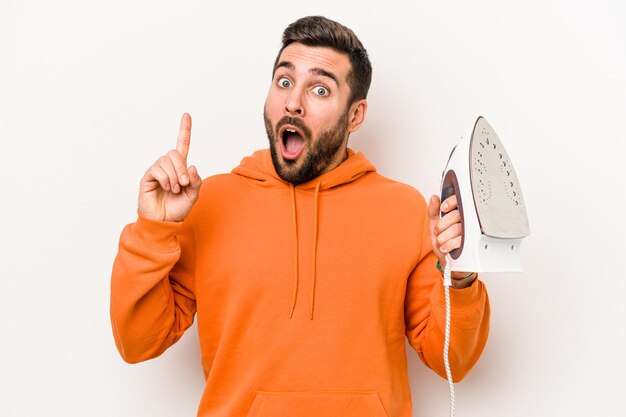 Young caucasian man holding an iron isolated on white background having an idea inspiration concept