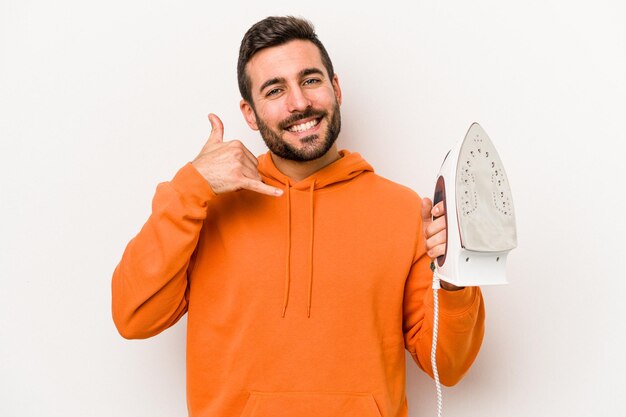 Young caucasian man holding an iron isolated on white background showing a mobile phone call gesture with fingers