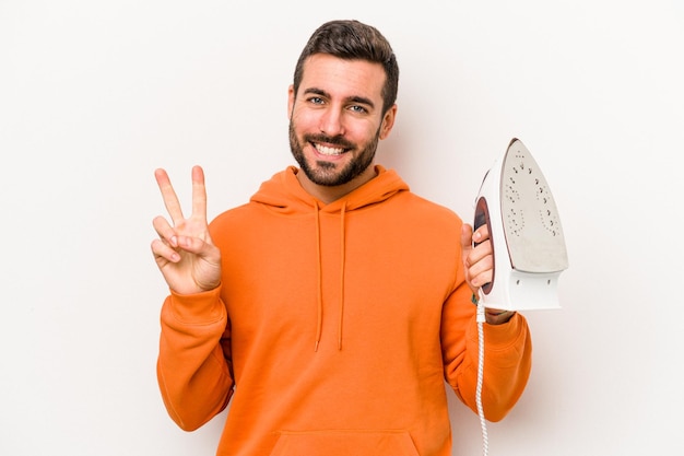 Young caucasian man holding an iron isolated on white background showing number two with fingers