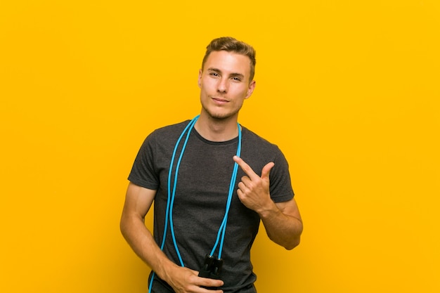 Young caucasian man holding a jump rope pointing with finger at you as if inviting come closer.