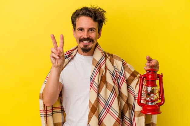 Young caucasian man holding lantern isolated on yellow background showing number two with fingers.