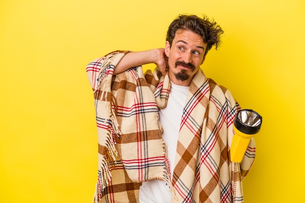 Young caucasian man holding lantern isolated on yellow background touching back of head, thinking and making a choice.