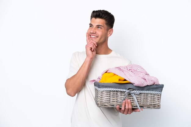 Young caucasian man holding laundry basket isolated on white background thinking an idea while looking up