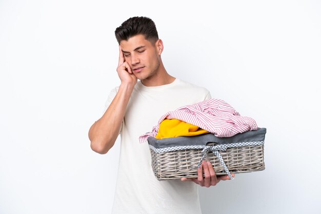 Young caucasian man holding laundry basket isolated on white background with headache