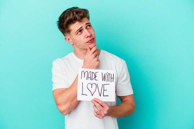 Young caucasian man holding a made with love placard isolated on blue