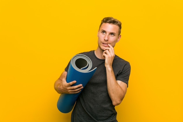 Young caucasian man holding a mat relaxed thinking about something looking at a copy space