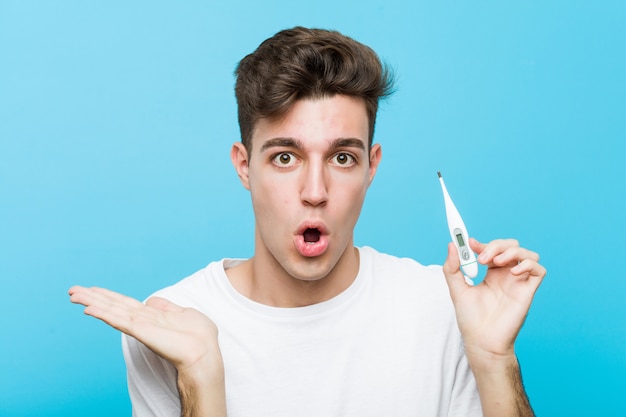 Young caucasian man holding a medical thermometer impressed