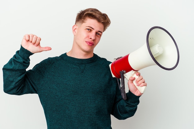 Young caucasian man holding a megaphone isolated on white wall feels proud and self confident, example to follow.