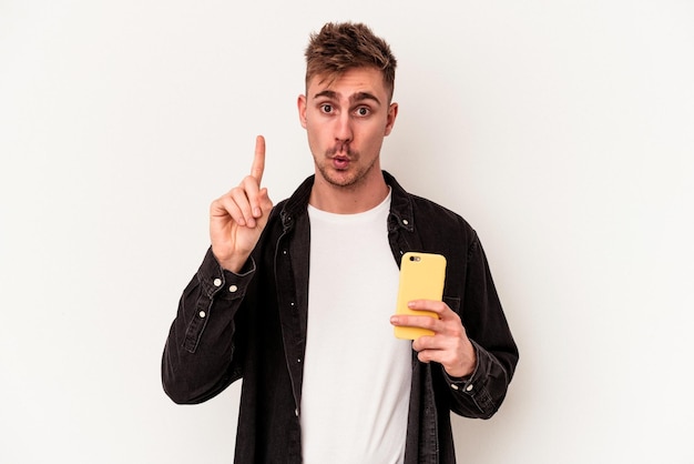 Young caucasian man holding a mobile phone isolated on white background having some great idea, concept of creativity.