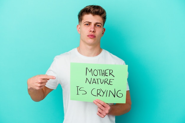 Young caucasian man holding a Mother Nature is crying placard isolated on blue wall