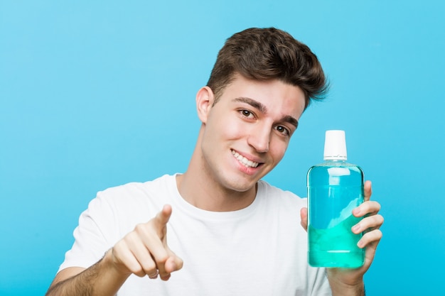 Young caucasian man holding a mouthwash cheerful smiles pointing to front.