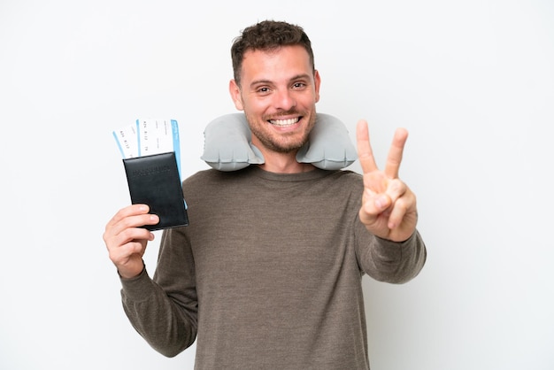 Giovane uomo caucasico in possesso di un passaporto isolato su sfondo bianco sorridente e mostrando segno di vittoria