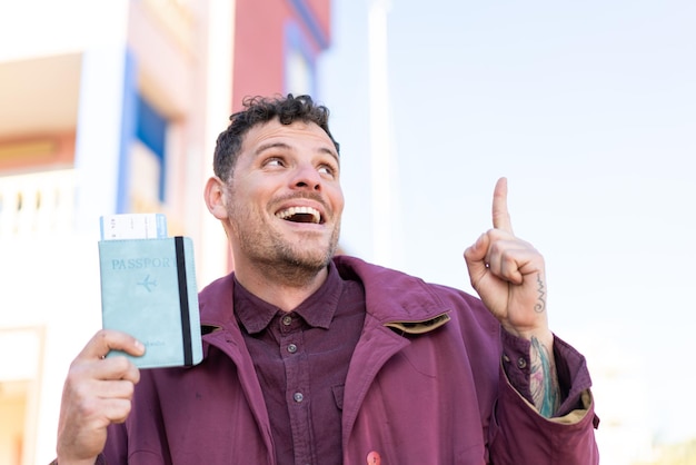 Young caucasian man holding a passport at outdoors intending to realizes the solution while lifting a finger up