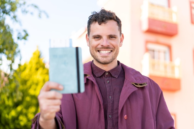 Photo young caucasian man holding a passport at outdoors with happy expression