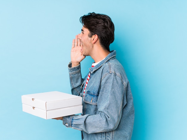 Young caucasian man holding pizzas isolated shouting and holding palm near opened mouth.