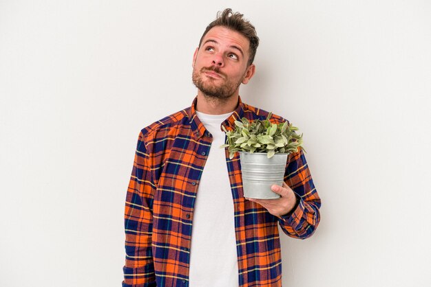 Young caucasian man holding a plant isolated on white background dreaming of achieving goals and purposes