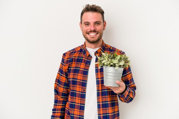 Young caucasian man holding a plant isolated on white background happy, smiling and cheerful.