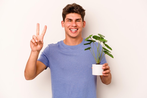 指で2番目を示す白い背景で隔離の植物を保持している若い白人男性
