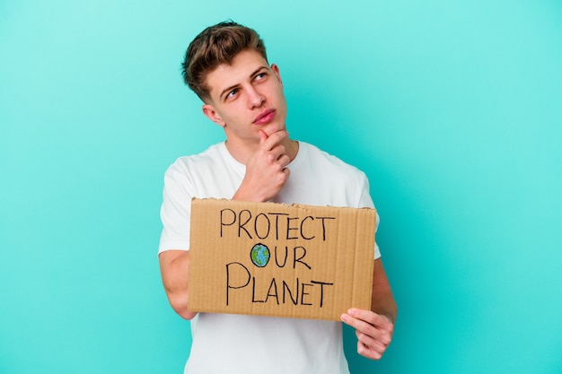 Young caucasian man holding a protect our planet placard isolated on blue wall